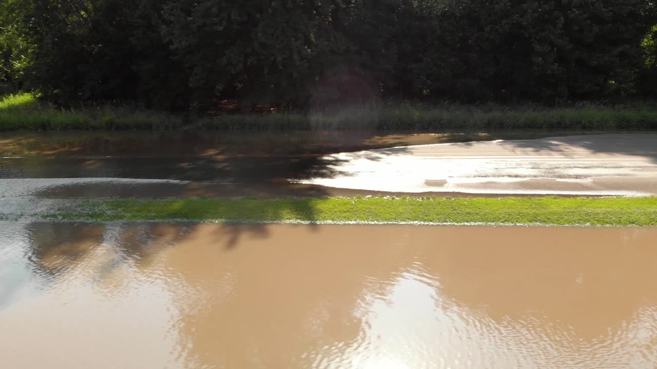 4k aerial view panning right to left showing flood water going over a road and road signs with sun reflection coming off the rippling water