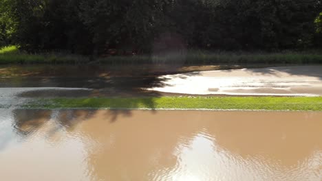 vista aérea de 4k panorámica de derecha a izquierda que muestra el agua de la inundación pasando por una carretera y las señales de tráfico con el reflejo del sol saliendo del agua ondulante