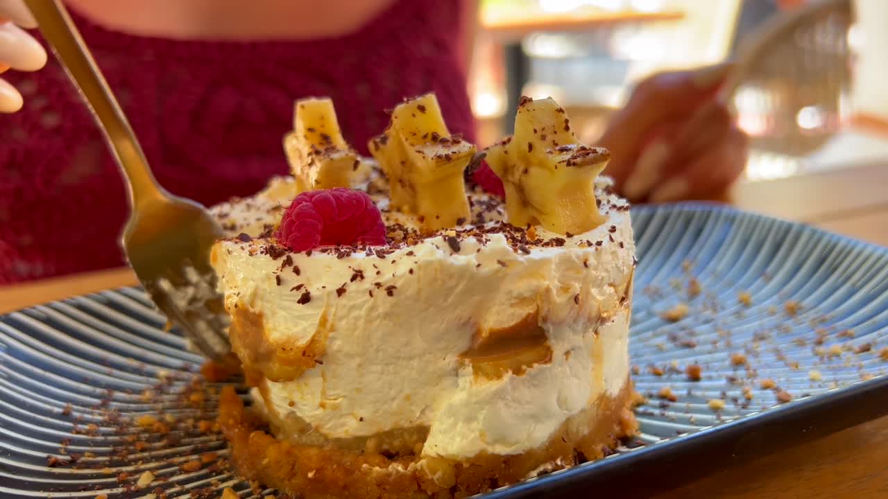 comiendo un delicioso pastel de banoffee con plátanos estrella, virutas de chocolate y frambuesas, una mujer disfrutando de un postre de pastel de crema dulce en un restaurante, toma de 4k