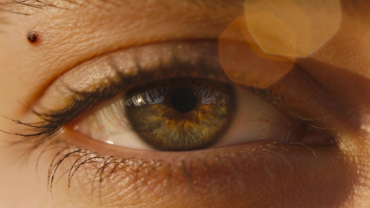 Donna che sbatte le palpebre reagendo a un cambiamento di luce, riaprendo l'occhio in primo piano, mostrando il riflesso sulla cornea e un neo