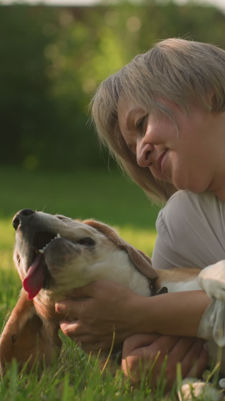 donna sdraiata con il suo cane su un campo erboso, toccando delicatamente e tenendo affettuosamente il suo cane, entrambi godendo di un momento di pace sotto la calda luce del sole, circondati da un verde rigoglioso