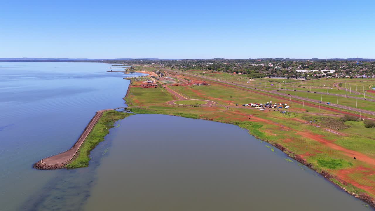 A wide aerial view of land reclamation and coastal development in Posadas, Misiones. The shot shows the red earth of new construction sites along a large lake or river