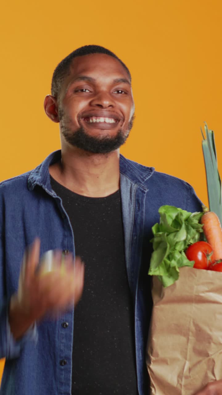 Uomo felice che fa il giocoliere con una mela mentre tiene in mano una borsa della spesa con prodotti freschi