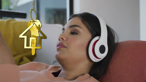 animation of gold house key and key fob over biracial woman using headphones at home