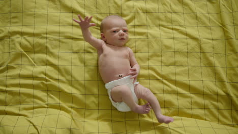 FULL-SHOT-TOP-DOWN---Newborn-baby-on-yellow-bedsheets-looking-at-the-camera