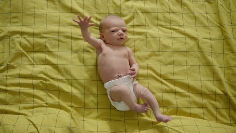 full shot top down - newborn baby on yellow bedsheets looking at the camera