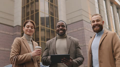 bottom view of caucasian businesswoman holding coffee, african american man watching to a tablet and caucasian man in the street in autumn