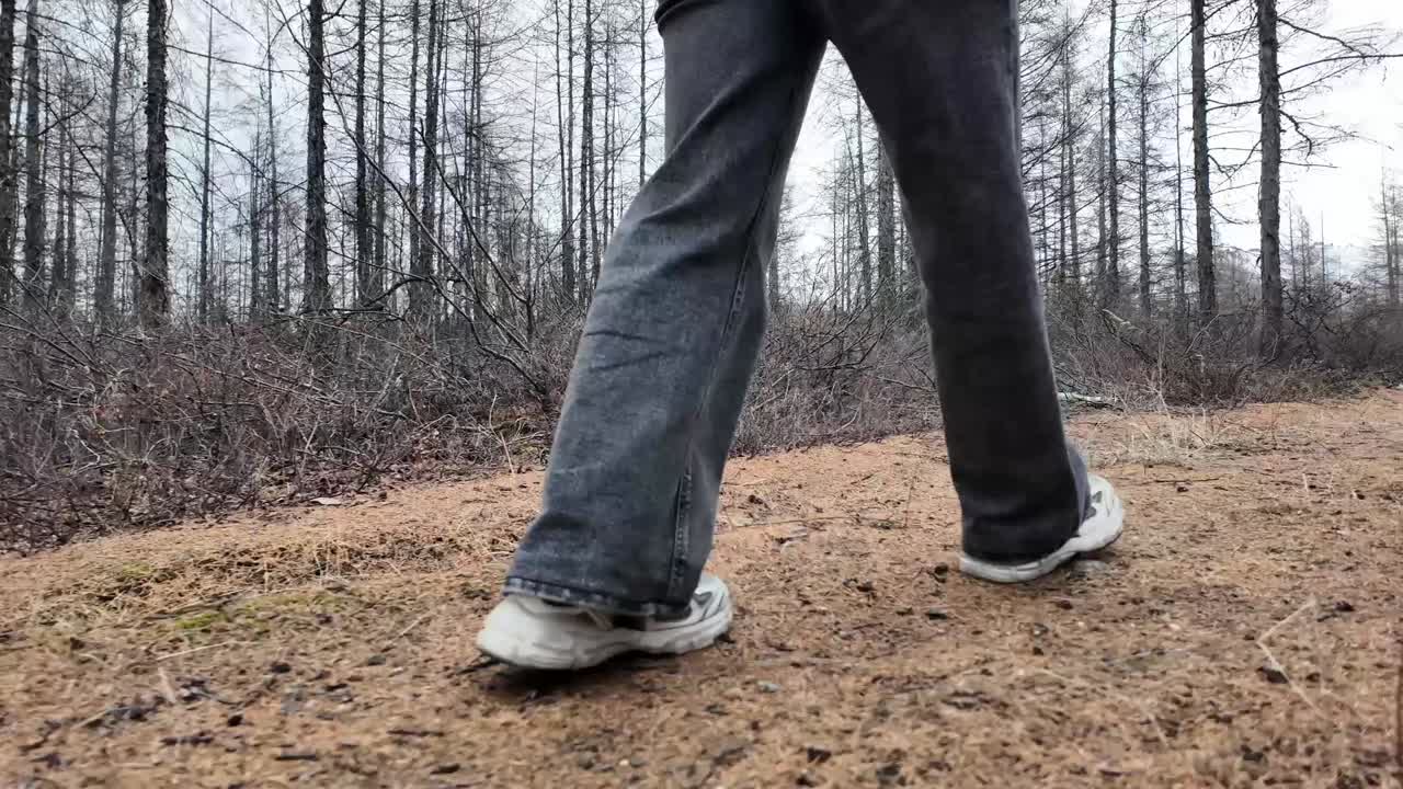 Kot pantolon ve spor ayakkabılarla orman patikasında yürüyen bir kişi