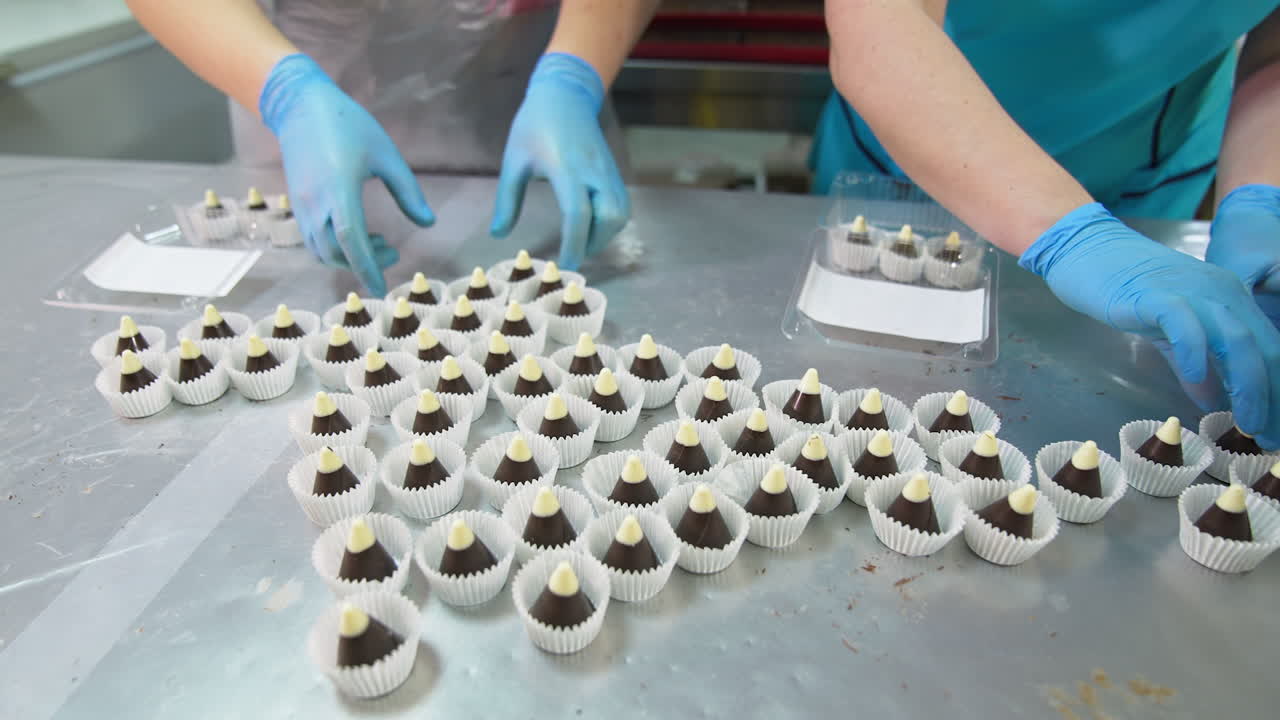 Beautiful delicious candy cones in individual wrapper are on the table. Workers in gloves put sweets into plastic boxes.