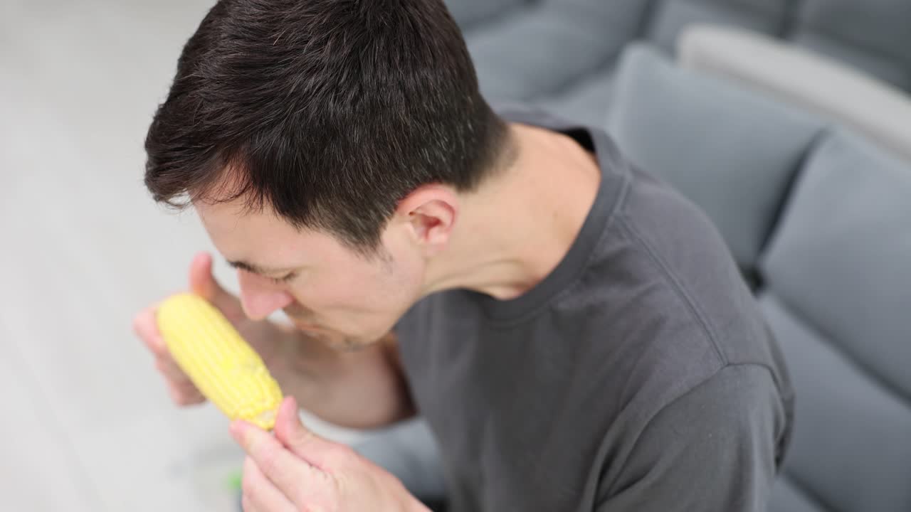 Man Eating and Holding Corn on the Cob at Home