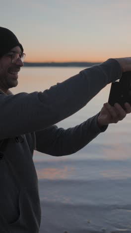 man taking photos by the water at sunset