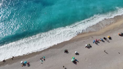 bird eye of white beach with umbrellas with blue water as waves are hitting the sand.