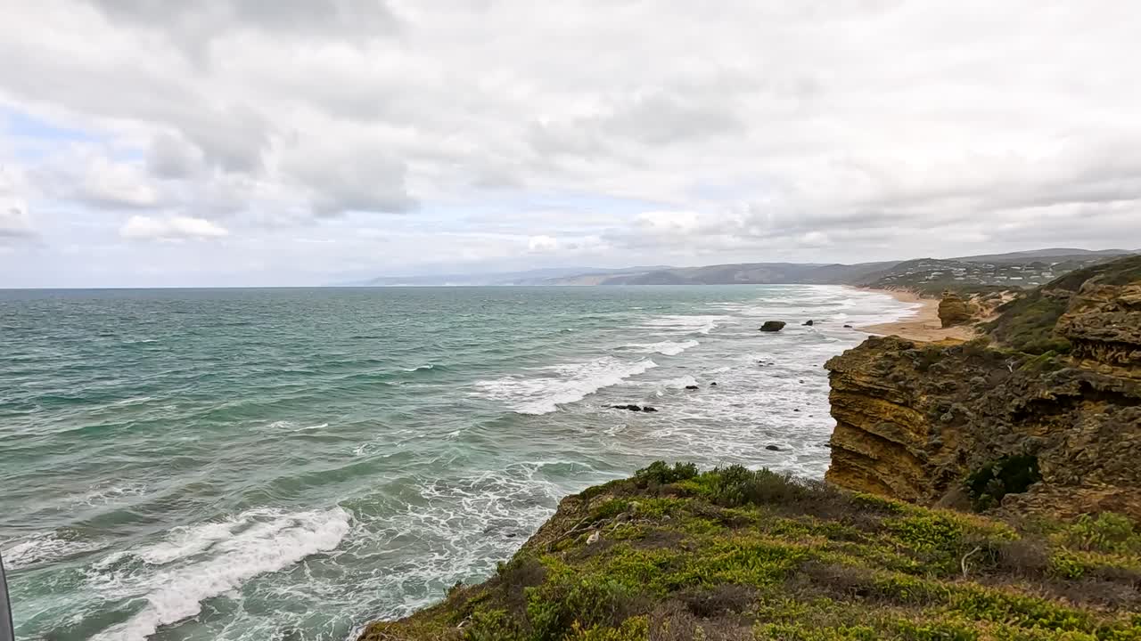 A breathtaking view of ocean waves crashing against rugged cliffs under a cloudy sky along Australia's Great Ocean Road
