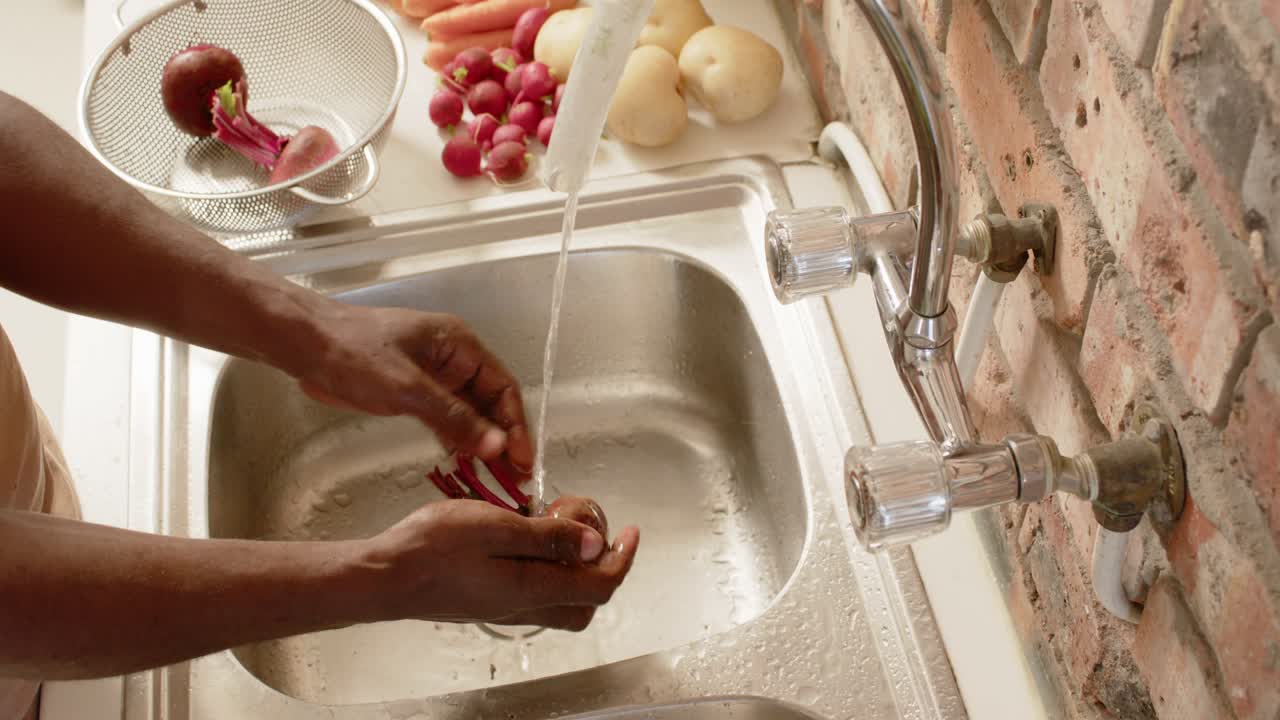 African man's hands turning on faucet, rinsing beetroot bunch at kitchen sink for cooking