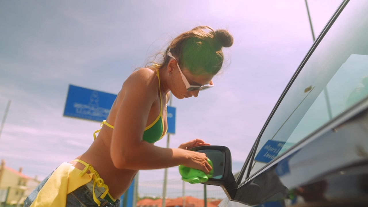 Young Woman in Bikini Cleaning Car Side Mirror on Sunny Day