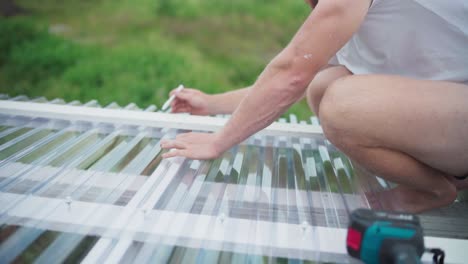 man puts on mark at the block of wood over corrugated polycarbonate roof of a greenhouse