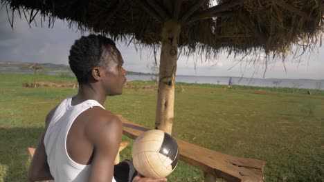 close up shot of a young african man relaxing on a beach hut by lake victoria while playing with a football