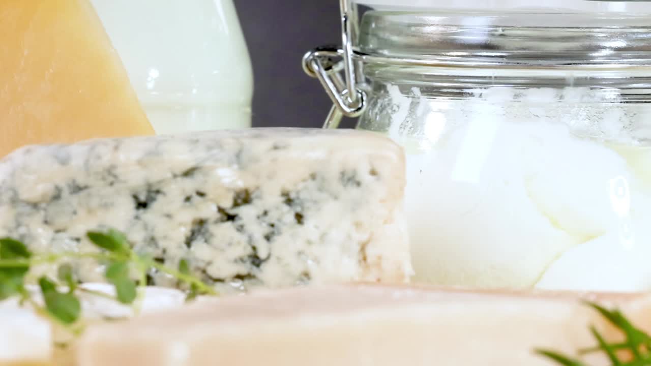 A variety of cheeses and dairy products in jars, beautifully arranged with herbs on a black background.