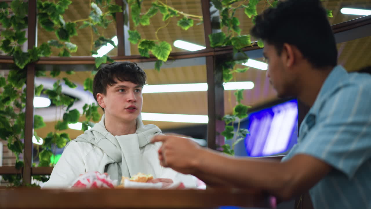Student in white shirt shaking head while looking at colleague during serious discussion , subtle background showing flowers hanging, emotional reaction conveying disagreement or concern