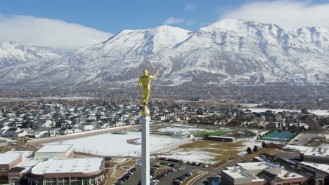 LDS-Mormon-Statue-on-Temple-by-Wasatch-Mountains-in-Utah,-Aerial-Orbit