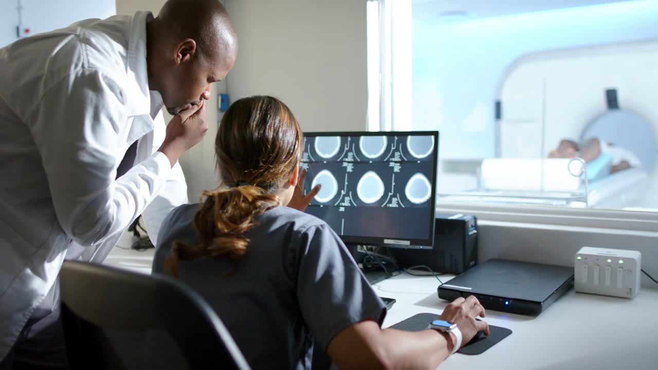 Physician and MRI tech consulting at console clicking mouse pointing at brain scans viewing patient