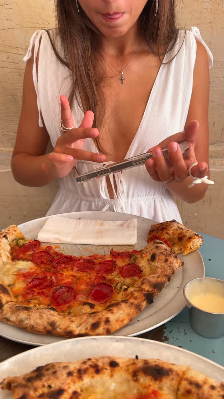 Woman at a restaurant with pizza, interacting with her smartphone