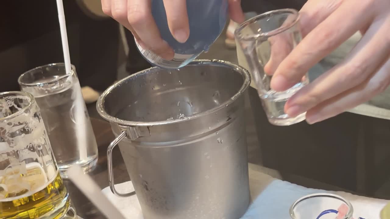 Un cameriere versa del sakè freddo da una bottiglia blu in un bicchiere in un ristorante
