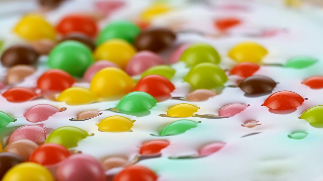 Caramelle colorate sparse sul latte, pezzi vivaci ricoperti di cioccolato che galleggiano in liquido cremoso, gusci lucidi
