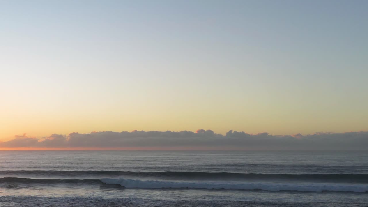 Calm ocean waves under a vibrant sunrise sky at Gold Coast, Australia. Soft lighting enhances the tranquil atmosphere
