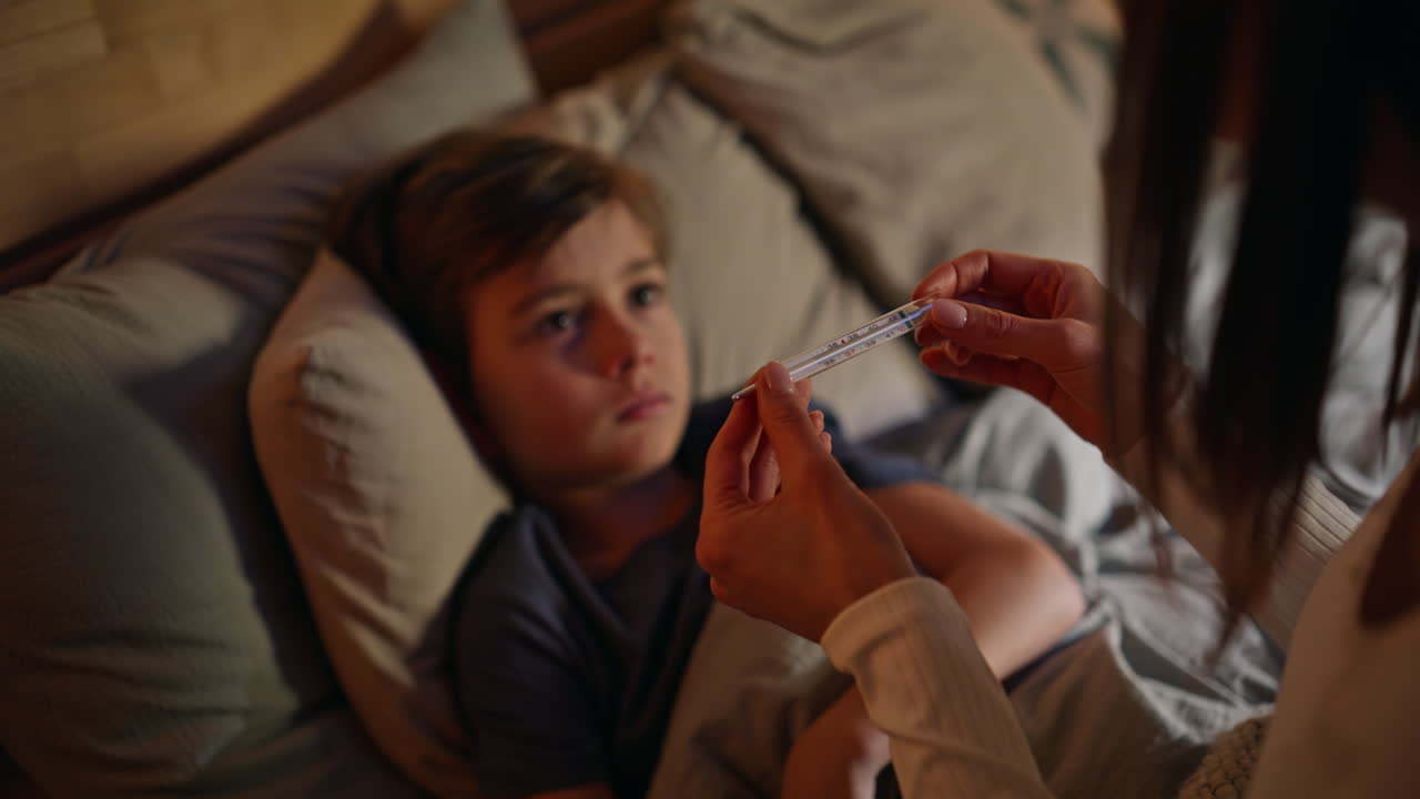 Mother hands checking thermometer caring health little boy lying bed closeup