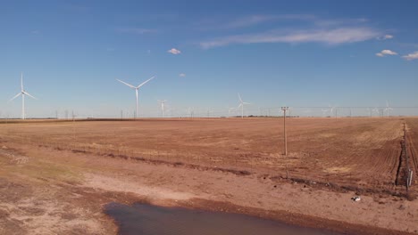 drone shot of spinning wind turbines, electric poles in a dry area