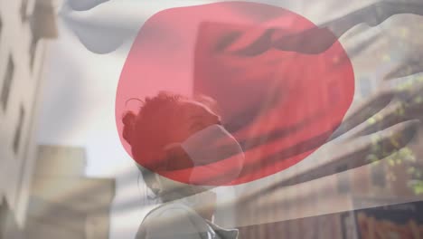 animation of flag of japan waving over african american woman wearing face mask in city street