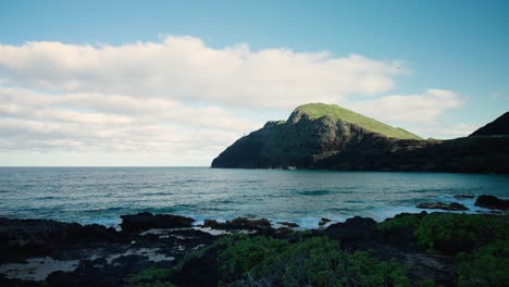 Sanft-Krachende-Wellen-Am-Ufer-Von-Oahu,-Hawaii-Mit-Gleitschirmen,-Die-Gegen-Einen-Malerischen-Blauen-Himmel-Mit-Wolken-über-Dem-Makapuu-Point-Leuchtturm-Gleiten
