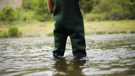 slow motion shot of a male fisherman wearing waders while fly fishing