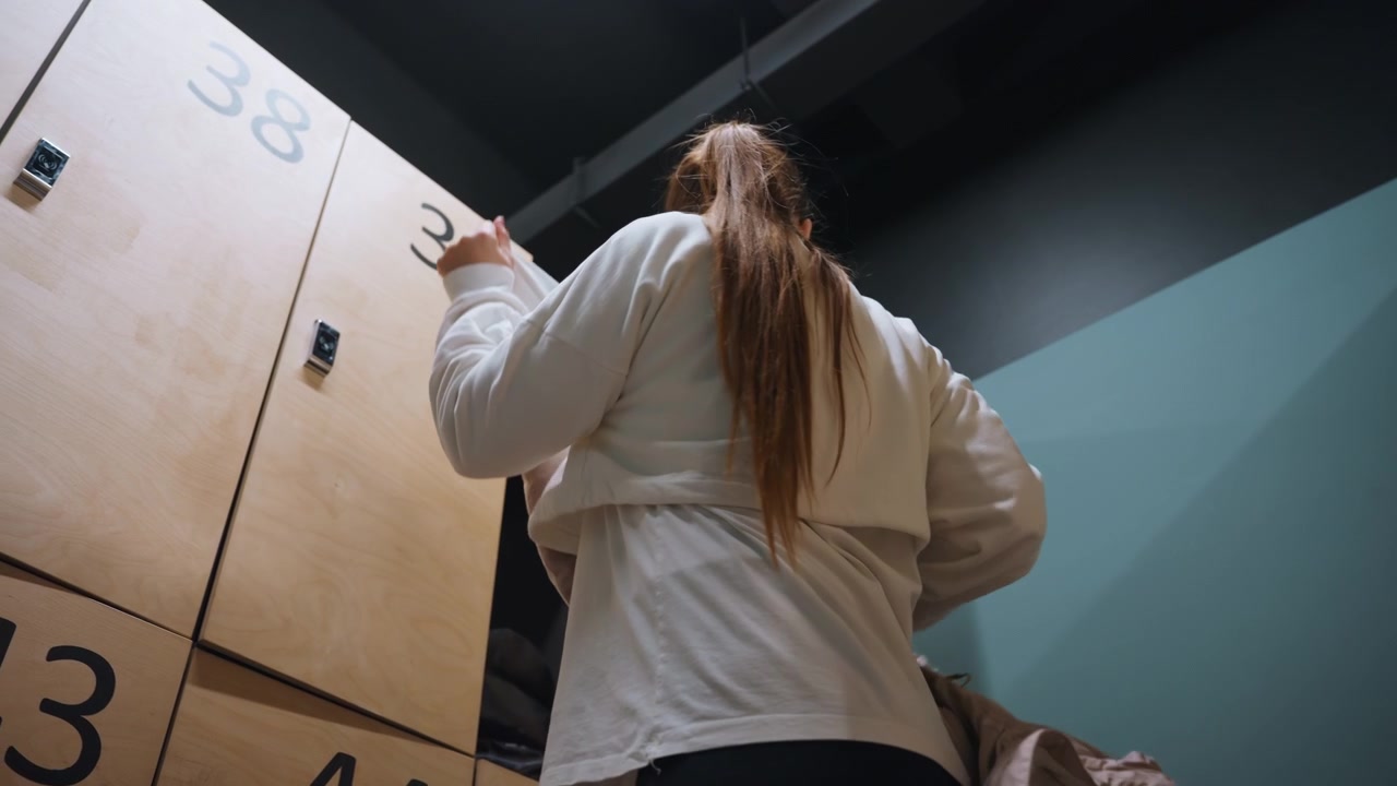 Gym prep scene. Woman opens locker calmly. Training preparation in quiet locker room. Serene scene of woman readying for badminton match. Peaceful moment of woman organizing gear in locker room