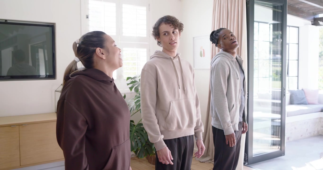 Diverse friends on cue doing neck stretches in living room near plant and window, easing tension