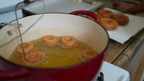 mini donuts frying in oil with larger donuts cooling in background, slowmo