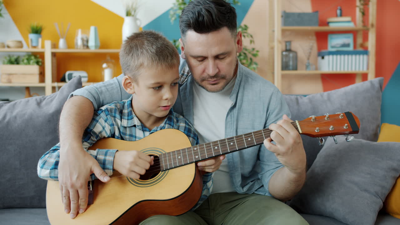 Father teaching his son how to play guitar at home.