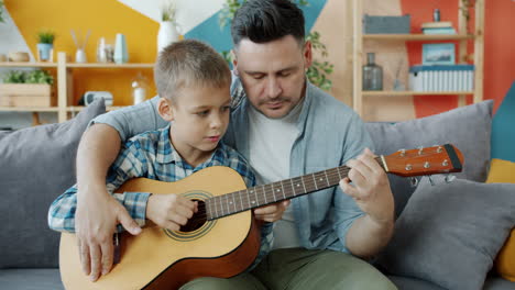 father teaching his son how to play guitar at home.