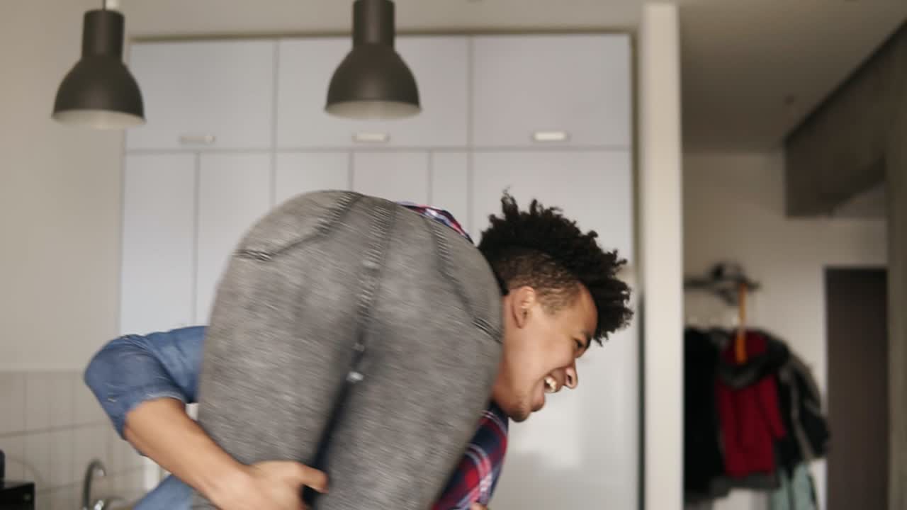 Cute happy couple. Handsome mullato guy lifts up and carries his laughing girlfriend around the apartment.