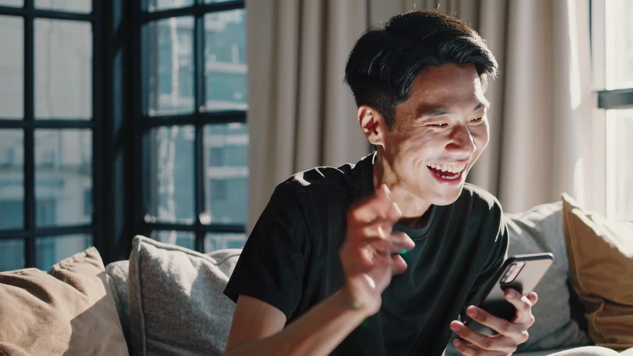 A young man smiling at his phone, captured in a close-up angle. The scene suggests a joyful moment