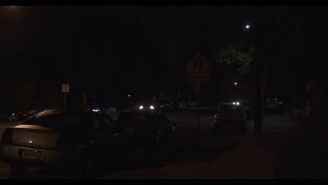 At-night-in-Los-Angeles,-on-the-street-near-the-courthouse-and-city-hall,-two-cars-pass-each-other-and-numerous-cars-are-parked-in-the-opposite-lane