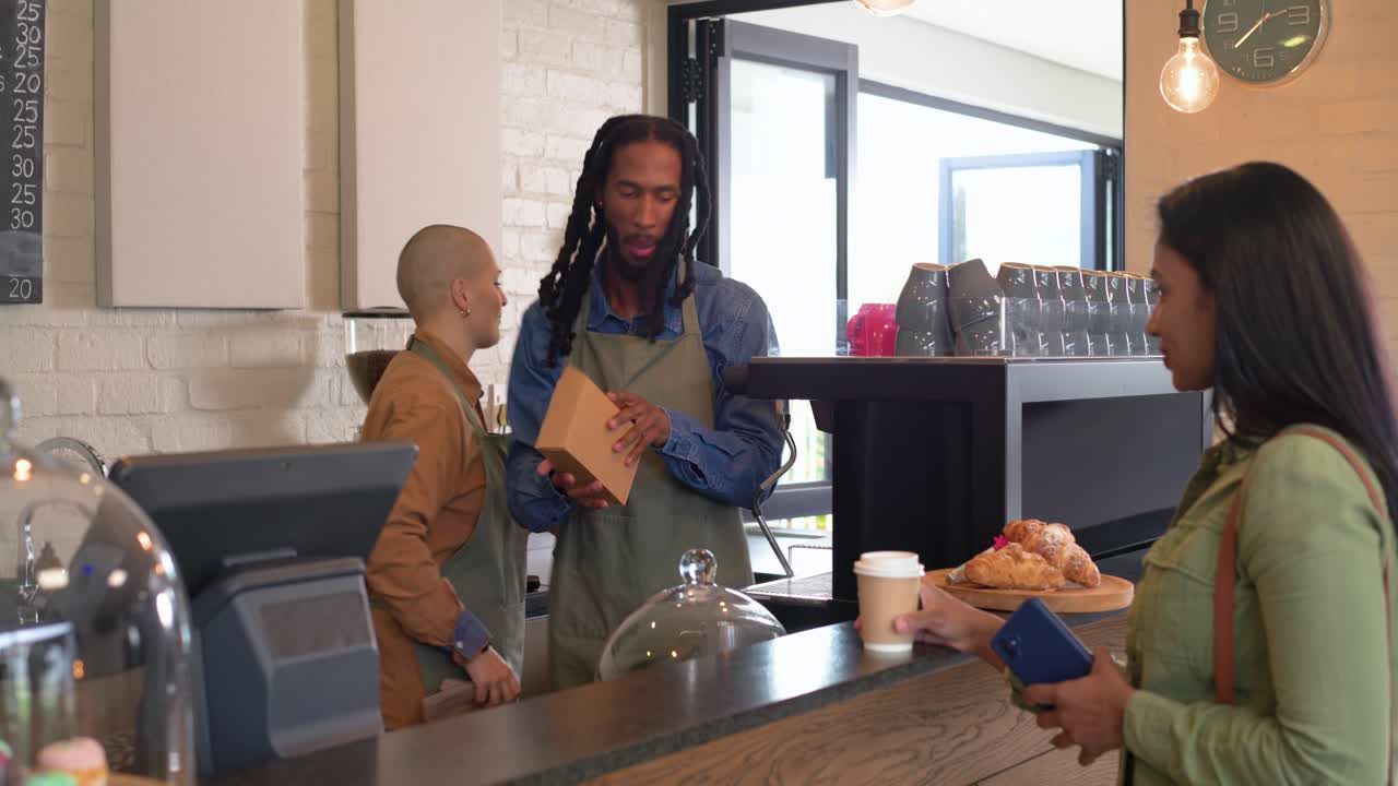 After customer ordering male barista serving coffee, selecting croissant, handing order at counter