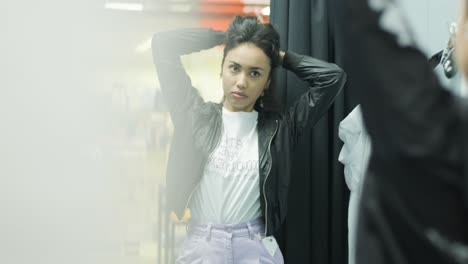 happy, stylish girl trying on outfit in dressing room in interior boutique clothing store with bright lighting.