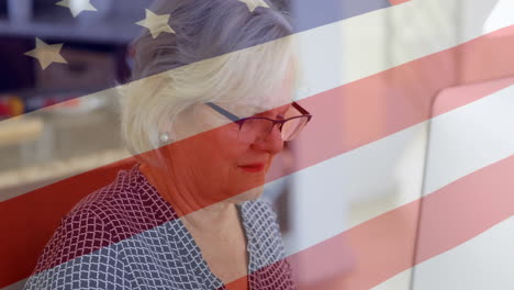 Animation-of-flag-of-usa-over-senior-caucasian-woman-using-laptop