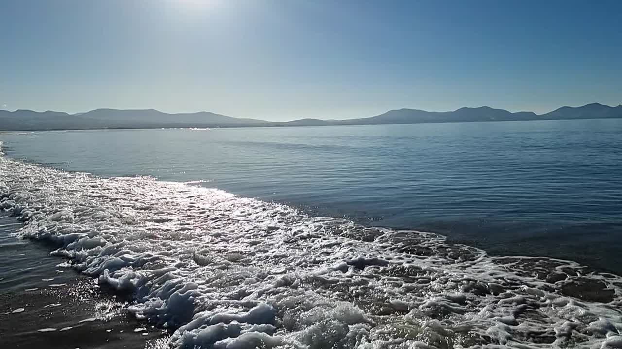 천천히 움직이는 조류 파도가 하늘의 흐릿한 해가 뜨는 스노우도니아 산맥의 스카이라인 아래  ⁇ 어