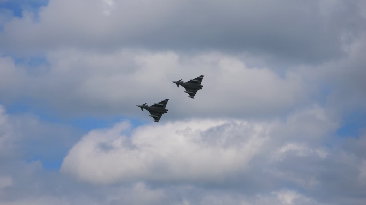 Two Eurofighters fly one behind the other in slow motion through the cloud-covered sky. Taken at the air show called Airpower 2024