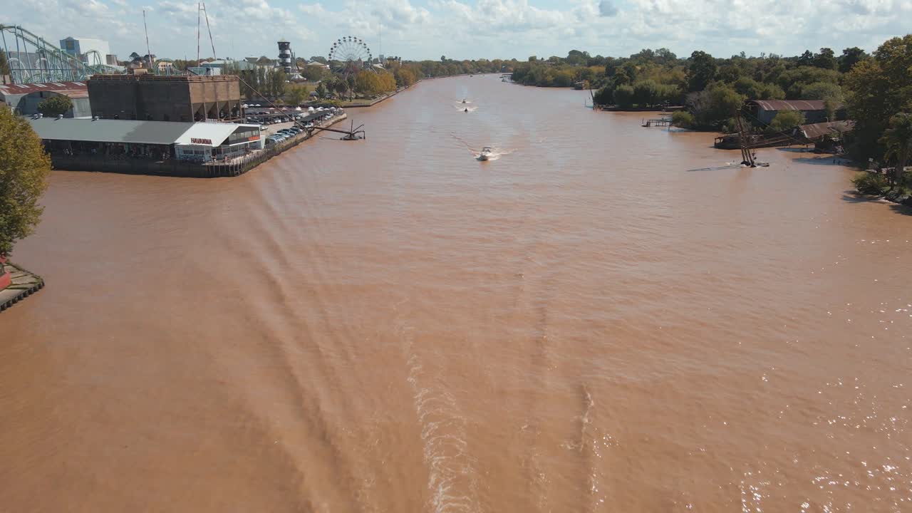 vista aérea volando sobre el río tigre con algunos barcos navegando y un parque temático en la parte trasera izquierda