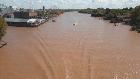 Aerial-view-flying-over-Tigre-river-with-some-boats-sailing-and-theme-park-at-left-back