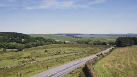 Aerial-high-to-low,-view-of-an-asphalt-road-through-the-rural-countryside-of-Dartmoor,-UK